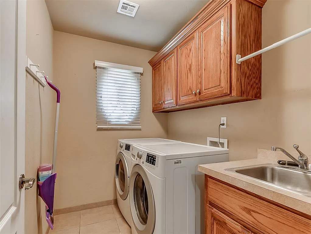 Custom laundry room with oak overhead cabinets, stainless sink, and finished tile floor