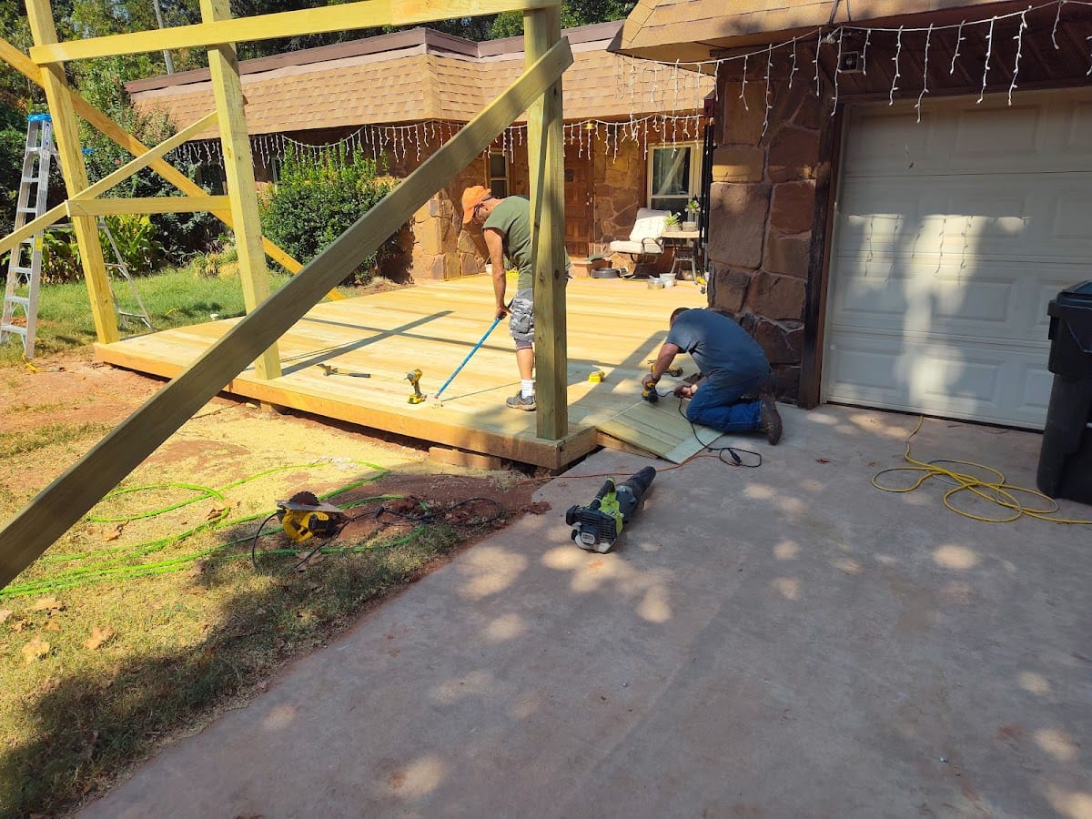 Carpenters building covered patio addition with stone-veneer home in background