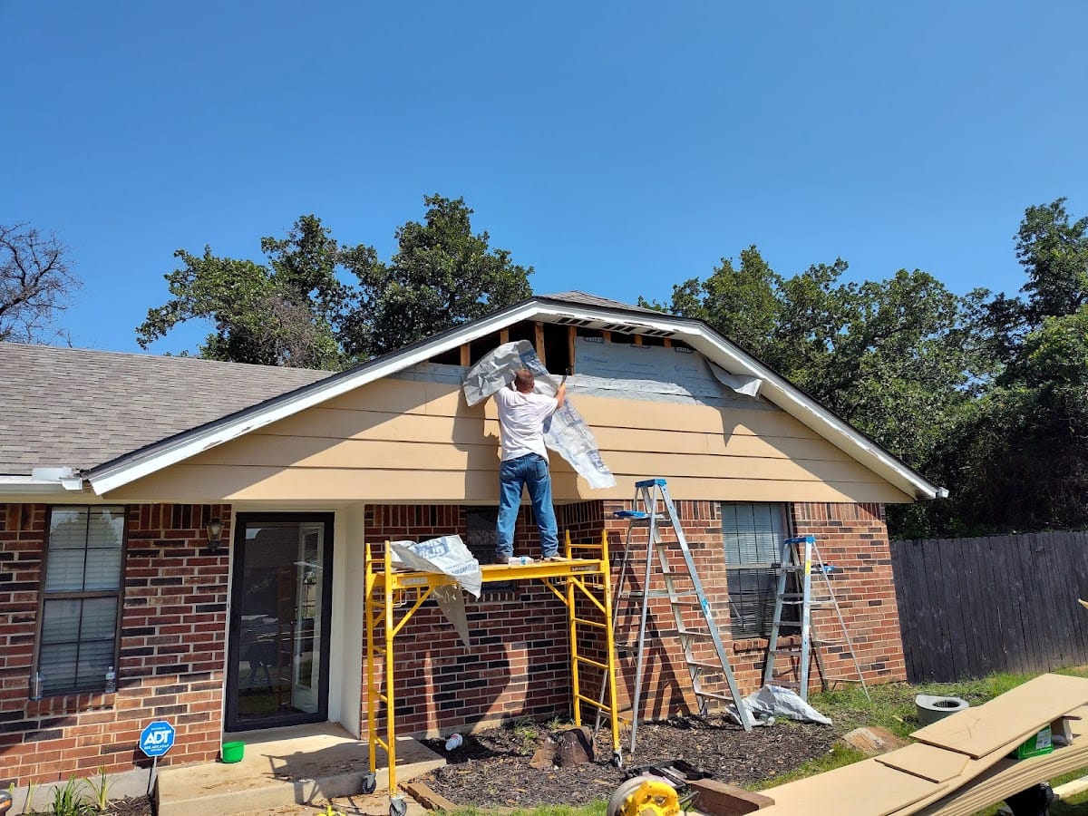 Worker on scaffold replacing siding on gable of brick home